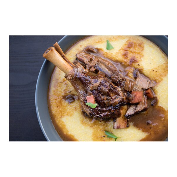 Beer-braised grass-fed lamb hindshank flecked with carrot & parsley in a blue bowl of polenta on black-stained wood background