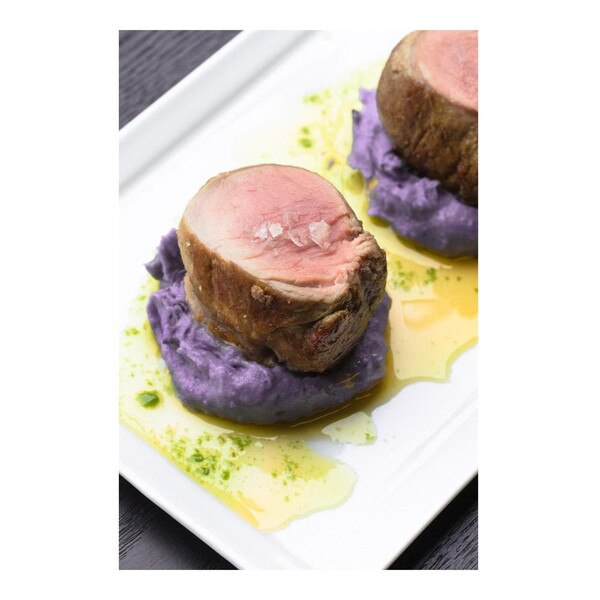 Cooked medallions of acorn fed Iberico pork tenderloin with purple potato puree & parsley oil on white plate