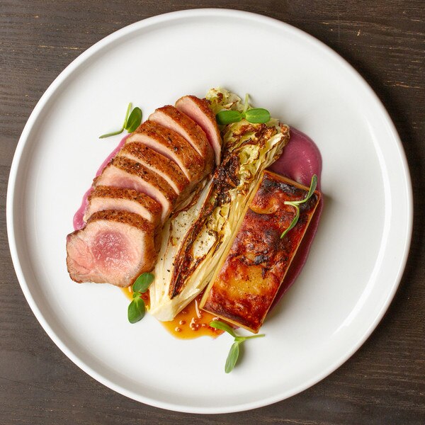 Cooked slices of Iberico pork striploin, charred cabbage, potato rectangle, green herbs, brown sauce on white plate