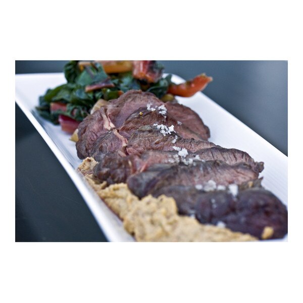 Grilled, sliced, boneless kangaroo loin, salt flakes, swiss chard, romesco sauce, rectangular white plate, blue background