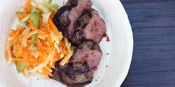 Grilled kangaroo medallions with fennel carrot slaw, white plate, blue wood background
