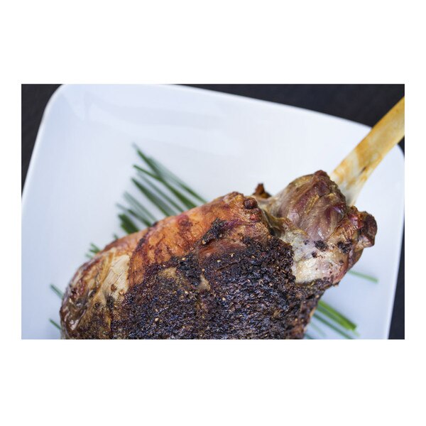 Cooked grass-fed lamb leg with bone exposed on a white plate with chives