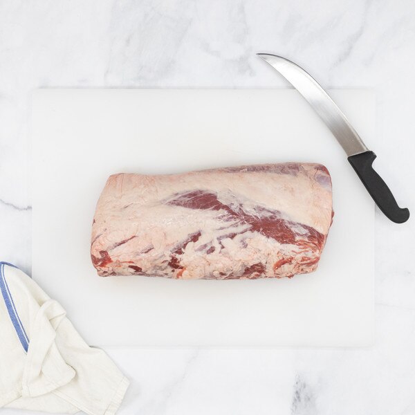 Raw Ocean Beef boneless ribeye roll on a white cutting board against a white marble background with a blue-striped towel, lower left, and a carving knife, upper right.