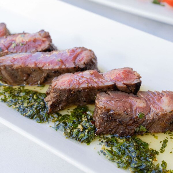 Cooked slices of Ocean Beef skirt steak lined up on a rectangular white plate sauced with a green herb sauce.