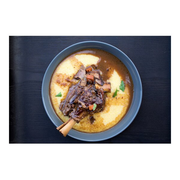 Beer-braised grass-fed lamb foreshank flecked with carrot & parsley in a blue bowl of polenta on black-stained wood background