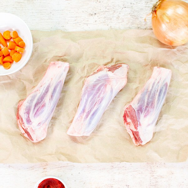 3 raw grass-fed lamb foreshanks with bowls of sliced carrots & tomato paste on brown butcher paper
