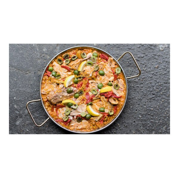 Paella with rabbit, red peppers, rice, lemon wedges, sliced olives in a round pan on a gray concrete background