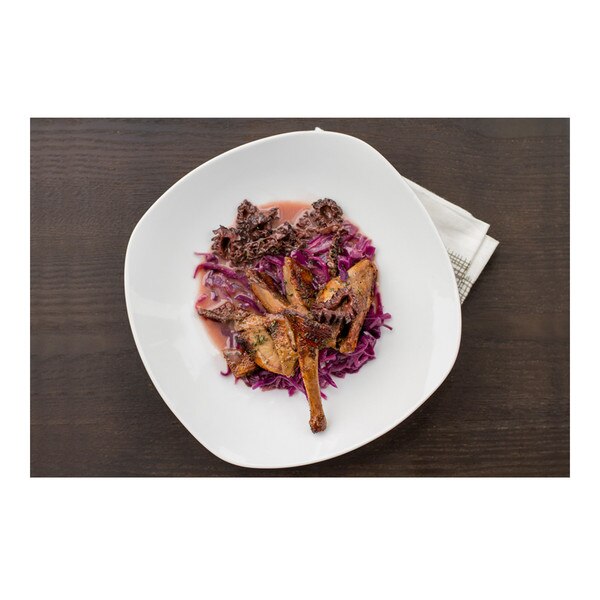 Split, seared squab with morels, red cabbage & pinot noir sauce on a white plate with napkin