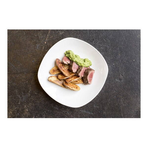Green sauce & roasted fingerling potato halves flanking 4 slices of cooked venison tenderloin on a square white plate